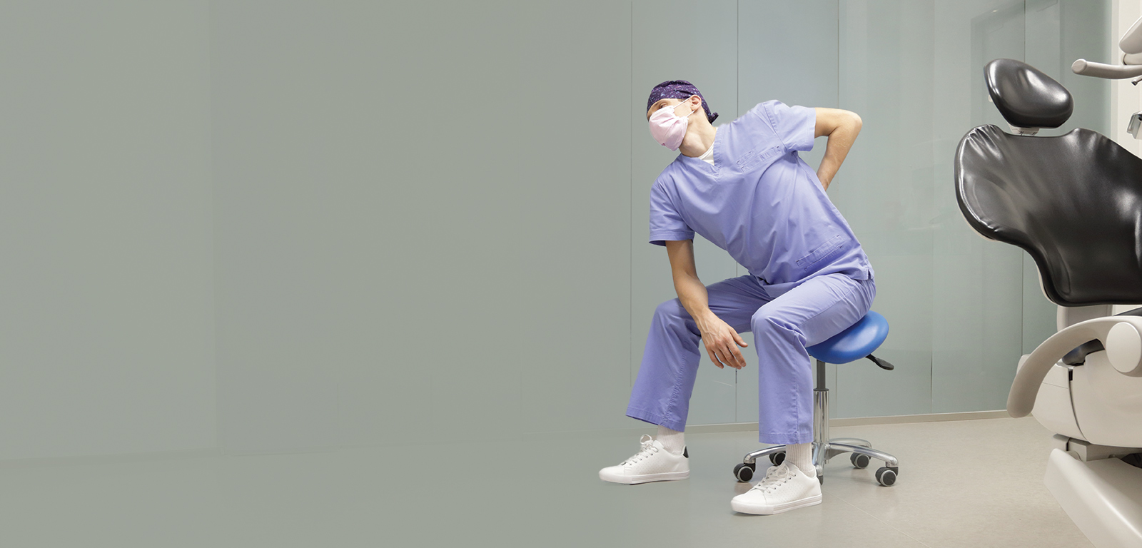 A dentist stretches his back while sitting on a surgical stool.