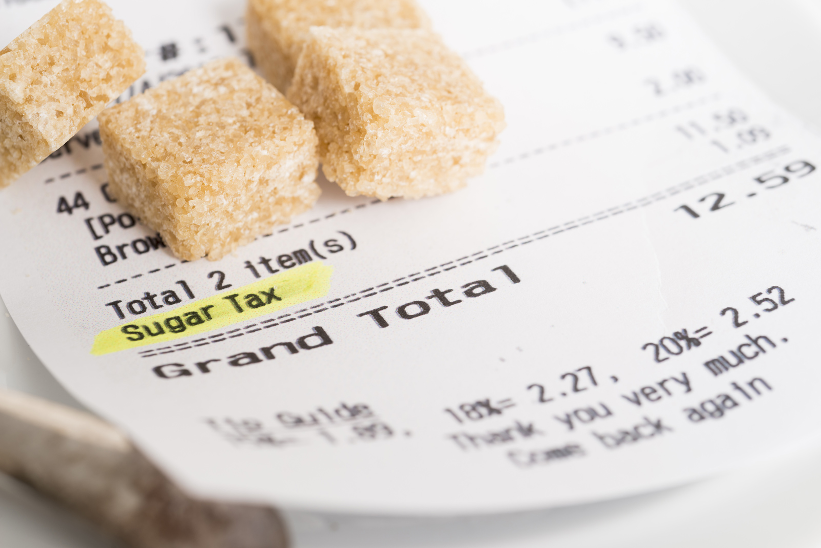 Four cubes of brown sugar sit on top of a super market reciept with an item labelled 'sugar tax' highlighted.