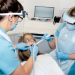 Two nurses stand either side of a patient in a dental chair.