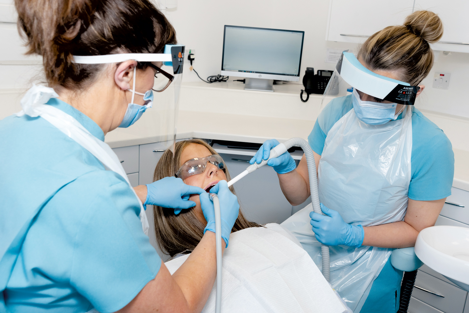 Two nurses stand either side of a patient in a dental chair.