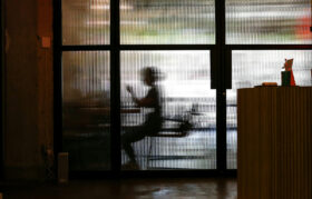 A person's frame can be seen through reeded glass with light beyond obscuring their identity.