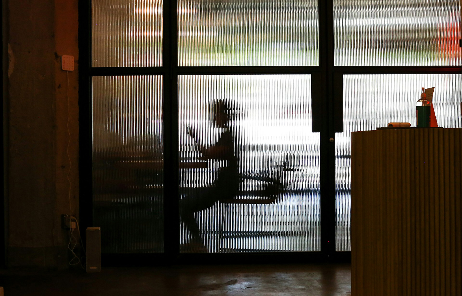A person's frame can be seen through reeded glass with light beyond obscuring their identity.