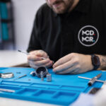 A technician sits at his workspace working on a task surrounded by tools.