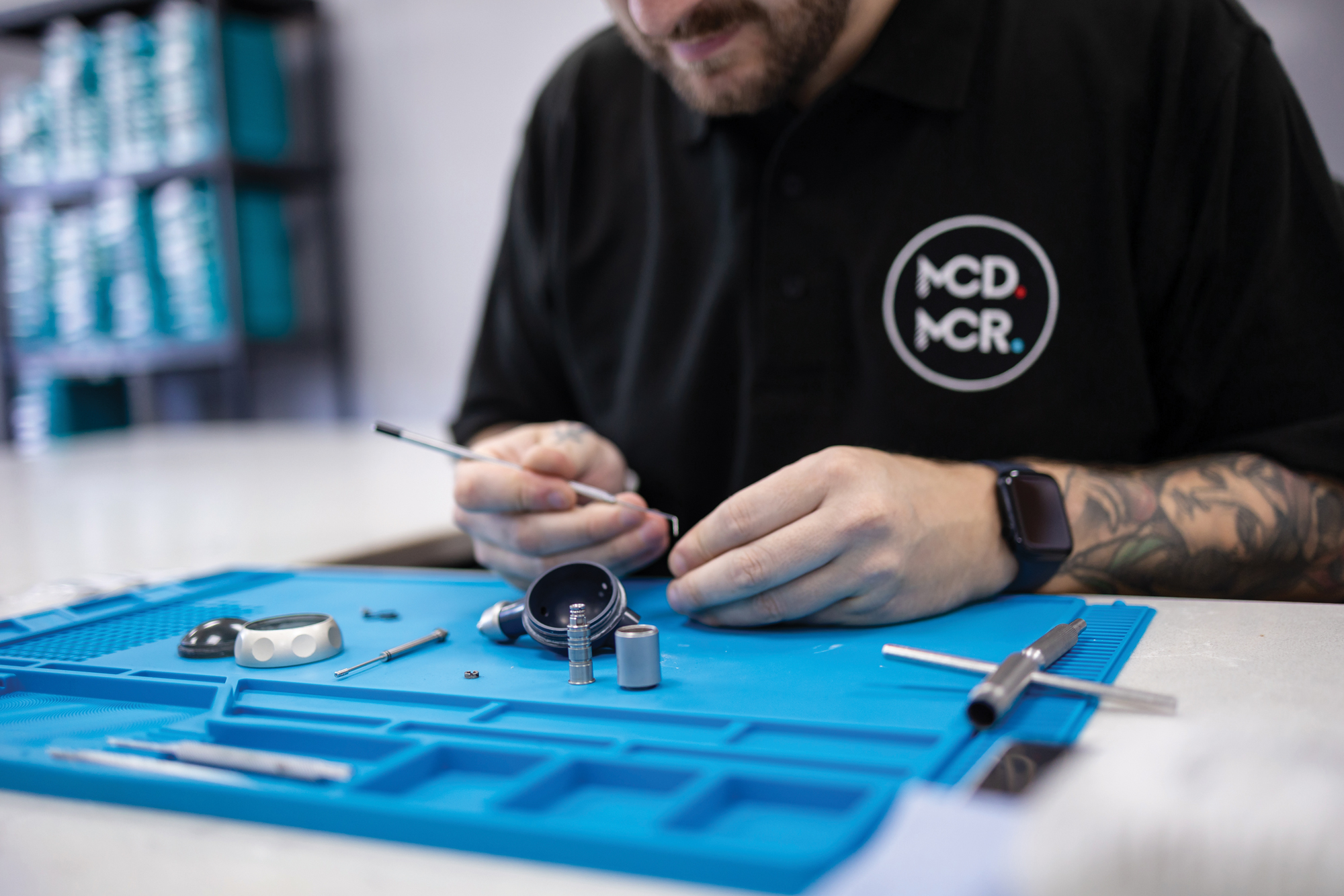 A technician sits at his workspace working on a task surrounded by tools.