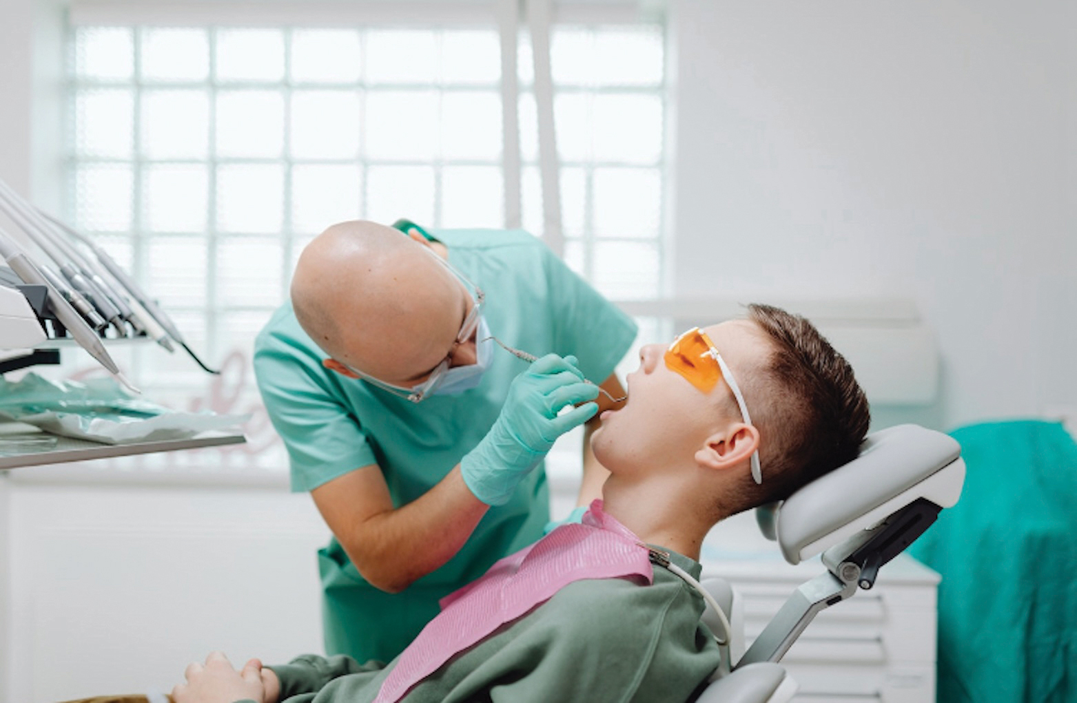 A dentist performs a check up on a patient while bent over at the hips.