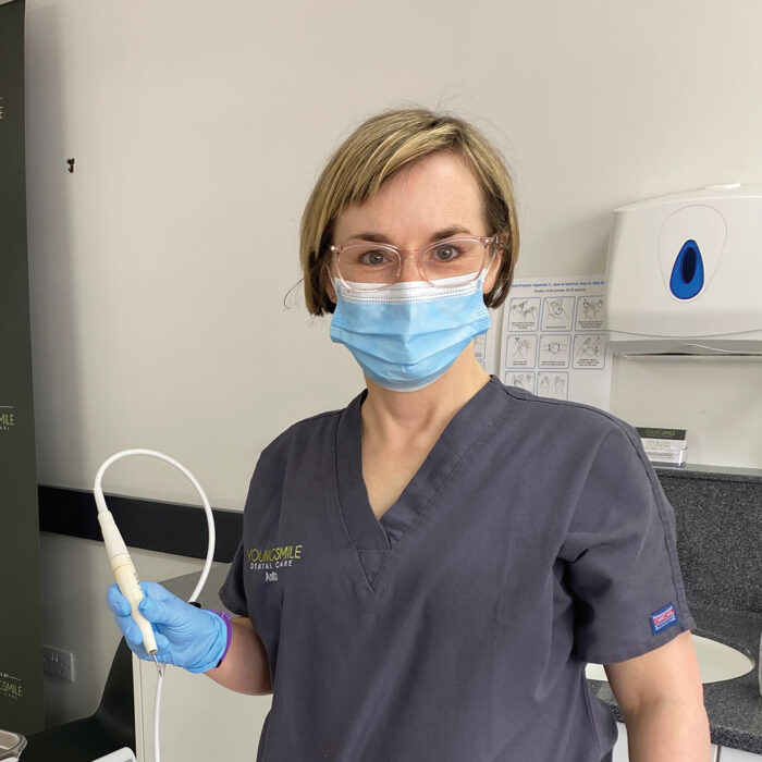 Anita holds a piece of dental equipment and wears a protective face mask in surgery.