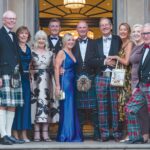 A group of people stand in a door way dressed in highland regalia for a photo