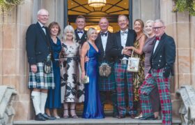 A group of people stand in a door way dressed in highland regalia for a photo