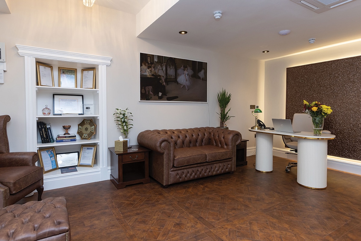 a large room with hardwood floors and leather sofa and chairs. A small white desk sits in the far corner.