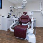 A spacious treatment room, with dark red dental chair fireplace and calm surroundings.