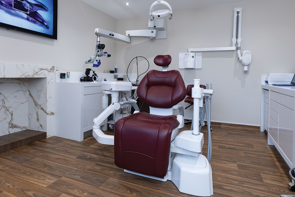 A spacious treatment room, with dark red dental chair fireplace and calm surroundings.