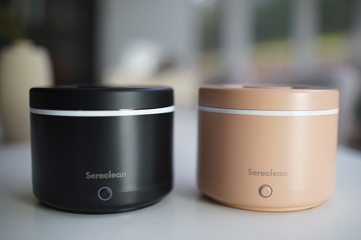 two round Sereclean pods with activation button on the front, one in black and one in tan.