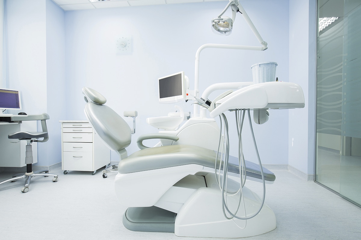 An empty dentist's chair in the middle of a brand new modern surgical room.