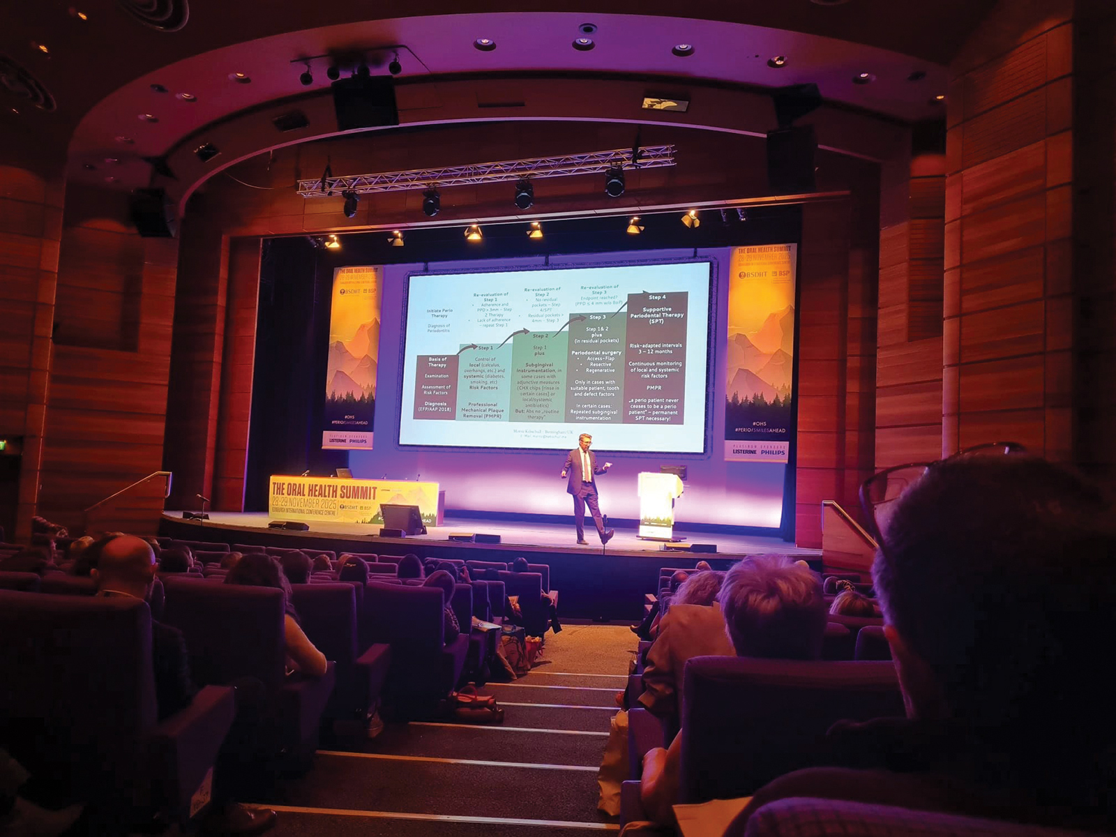 Professor Kebschull walks across stage in a darkened theatre.