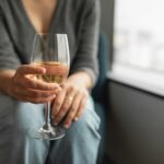 A woman leans forward holding a glass of white wine.