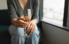 A woman leans forward holding a glass of white wine.