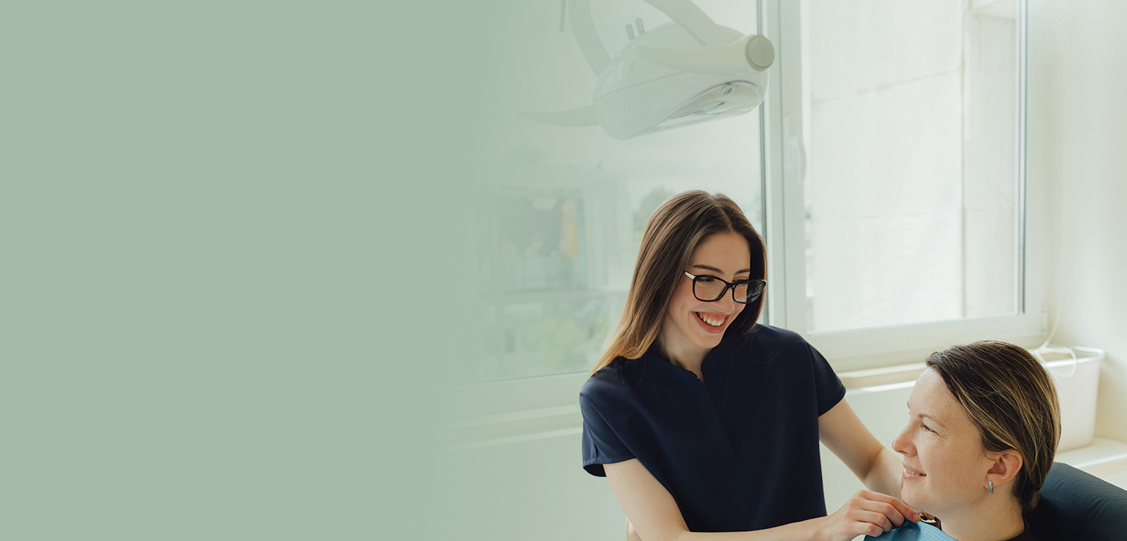 A female dentist smiles at her patient in a bright and airy surgery.