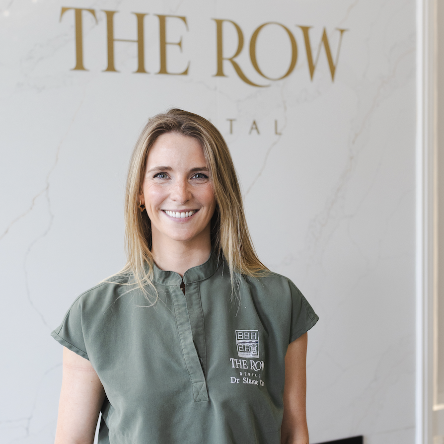 Dr Slaine Ker stands in front of a wall mounted logo for The Row Dental.